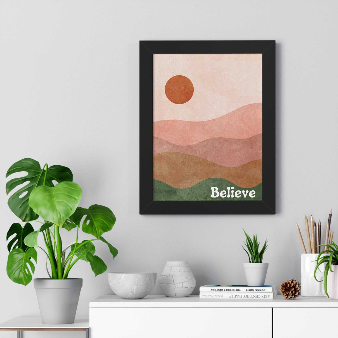 Framed Believe poster with abstract landscape and inspirational message hanging above white shelf with plants and decor