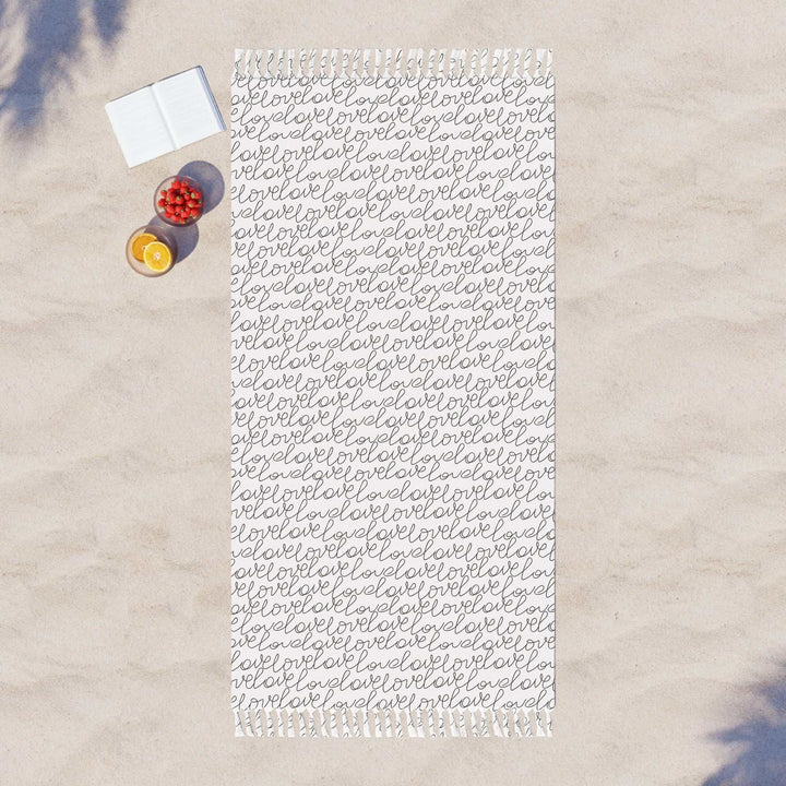 Large Love Beach Cloth with repeated script pattern on sand with book and fruits nearby
