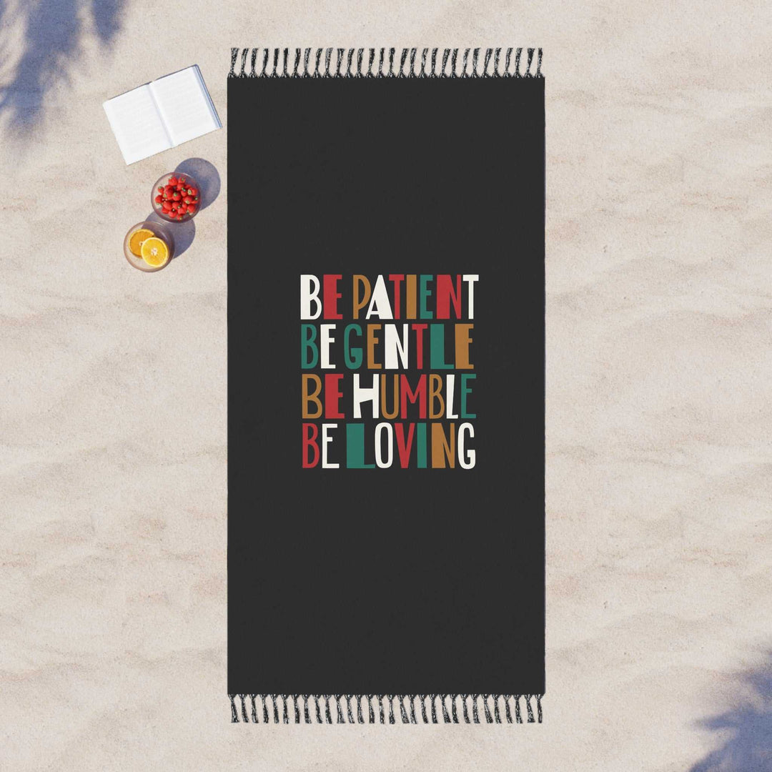 Bible Verse Beach Cloth with colorful "Be Patient Be Gentle Be Humble Be Loving" text on black polyester fabric with knotted tassels on sand background