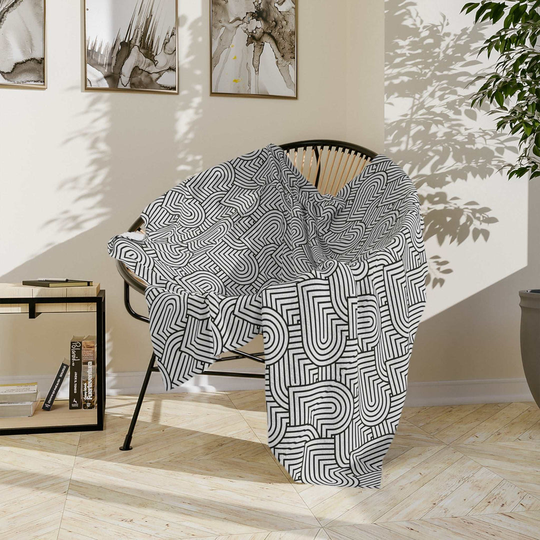 Black and white geometric patterned fleece blanket draped over chair in sunlight-filled room