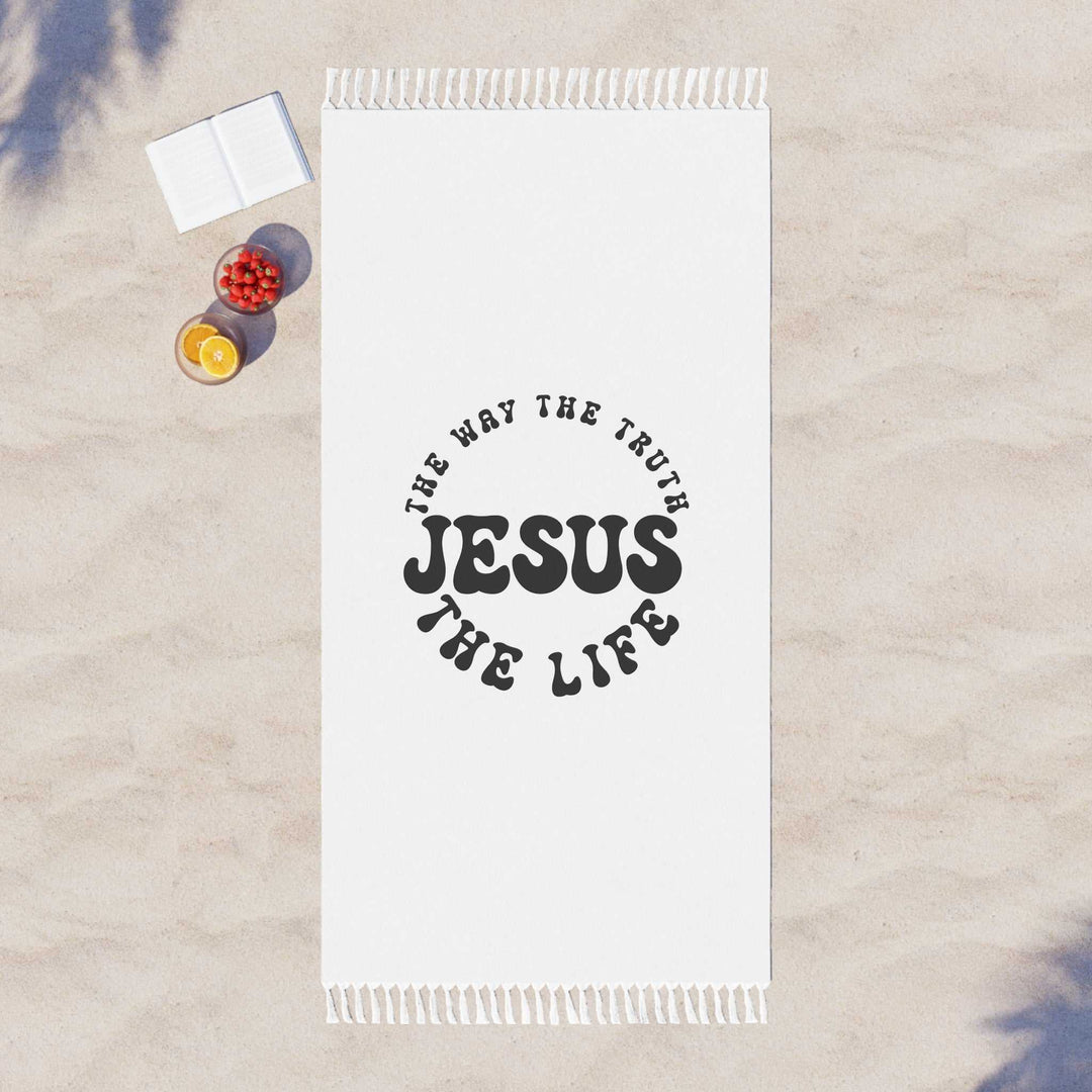 White Jesus Beach Cloth with knotted tassels, black faith-inspired text design, laid out on sandy beach with book and fruit bowls nearby