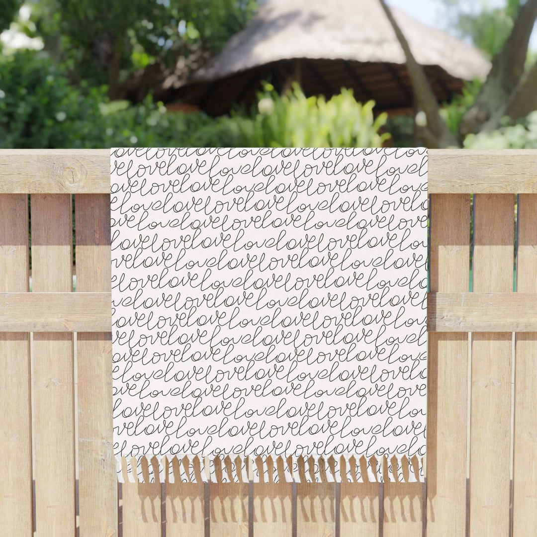 Love Beach Cloth with scripted pattern and knotted tassels hanging on wooden fence outdoors