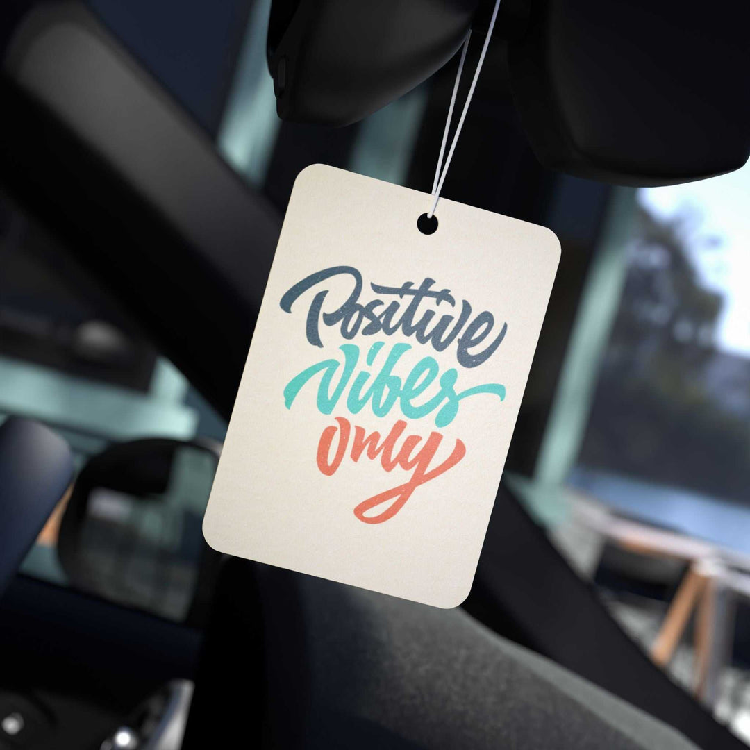 Positive Vibes Only car air freshener hanging inside a car with colorful text design and fresh scent options