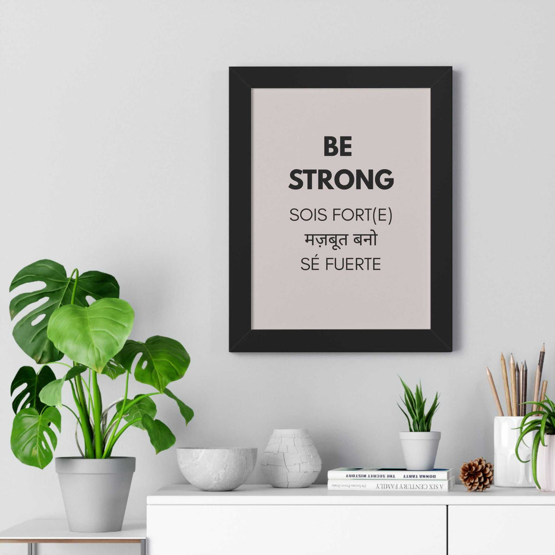 Framed motivational "Be Strong" poster in multiple languages displayed on a wall with modern decor and plants