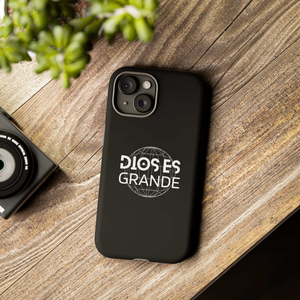 Black Dios Es Grande phone case with white text and globe design on wooden surface, durable dual-layer protective cover