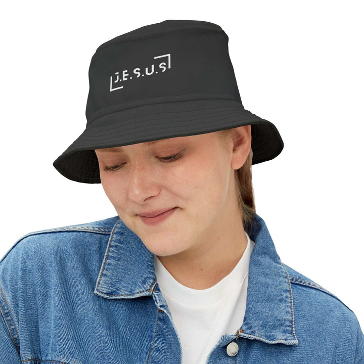 Black Jesus bucket hat with white lettering worn by a smiling person in a denim jacket