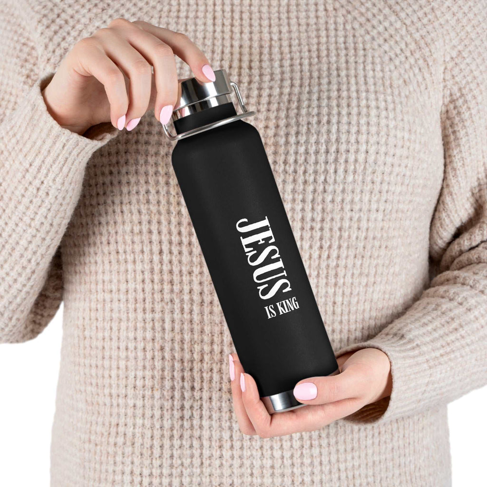Black "Jesus Is King" stainless steel bottle held by a person wearing a beige knit sweater.