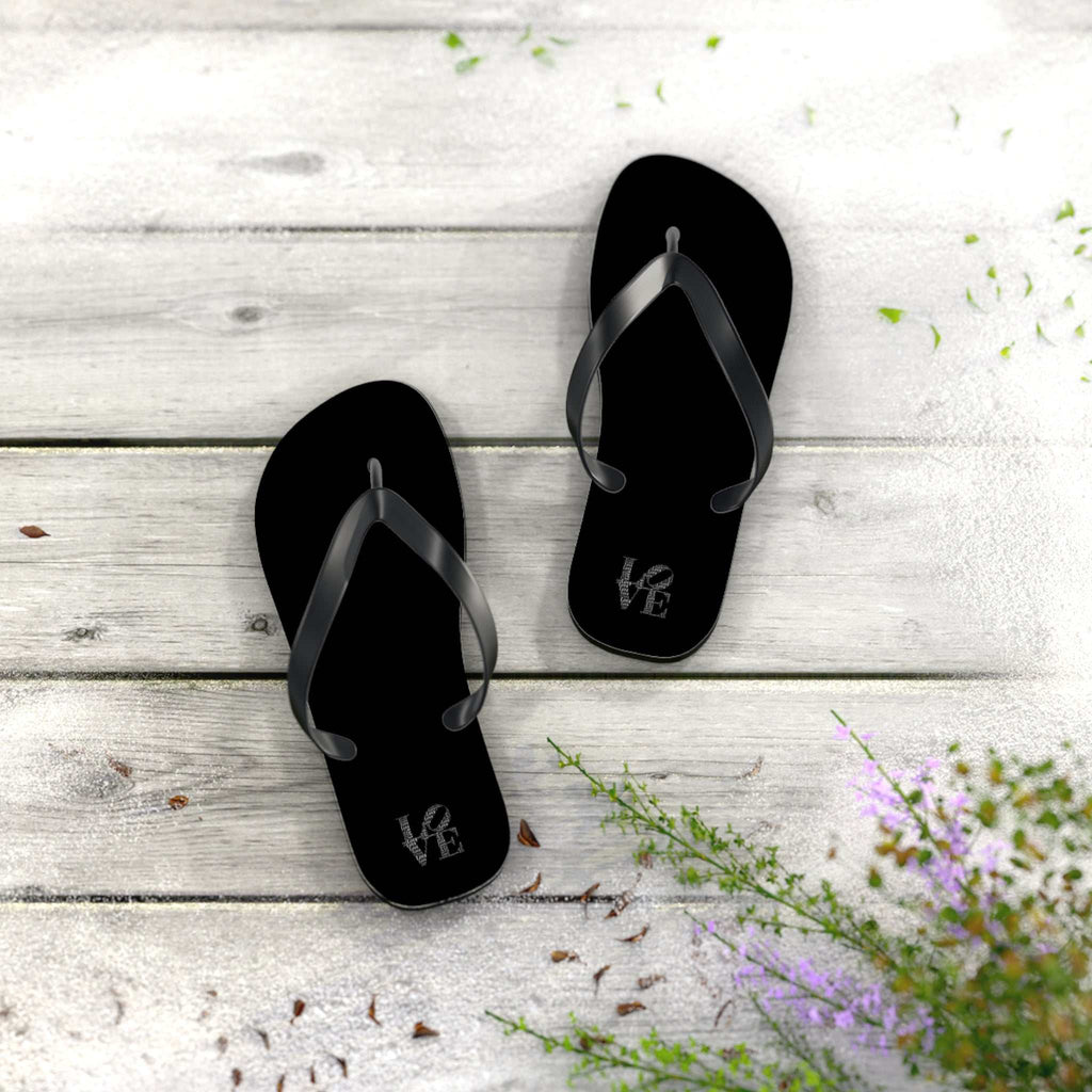 Black Love flip flops with cushioned sole on wooden surface