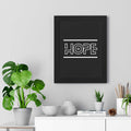 Black framed poster with the word "HOPE" in white modern typography hanging on a light gray wall above a white table with green plants and decorative objects