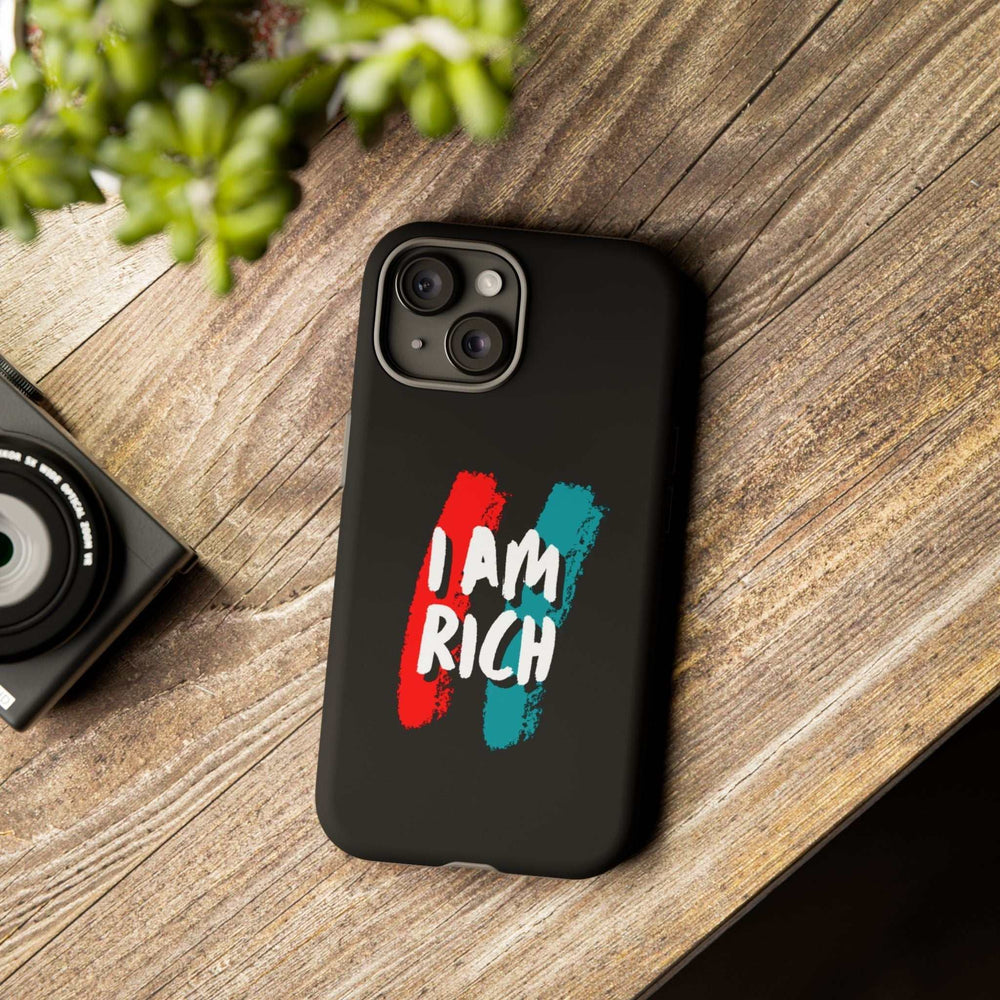 Black matte phone case with "I AM RICH" text in red and teal brush strokes, dual layer protective design