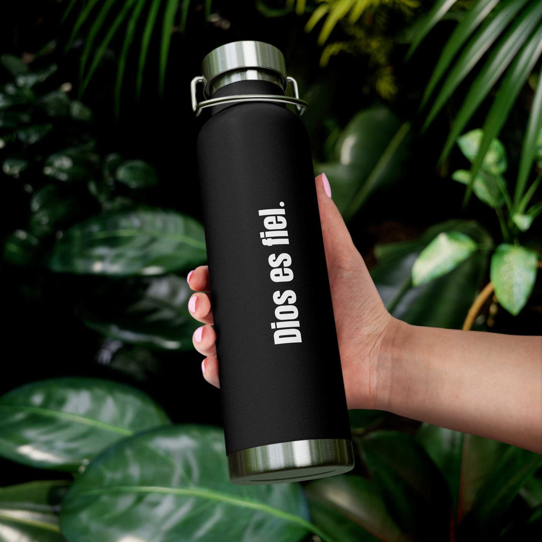 Black Dios Es Fiel bottle with silver cap held in hand against green foliage background
