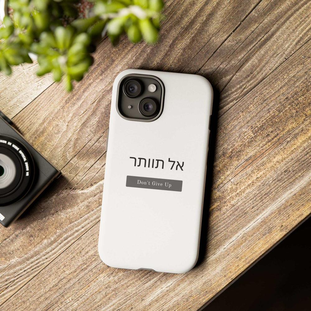 White "Don't Give Up" phone case with Hebrew text and matte finish on wooden surface, durable dual-layer protection design.
