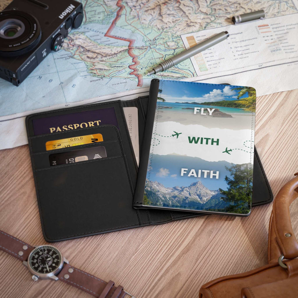 Black PU leather Fly with Faith passport cover with inner card slots and scenic mountain and beach design on front, placed on wooden surface with travel map and camera