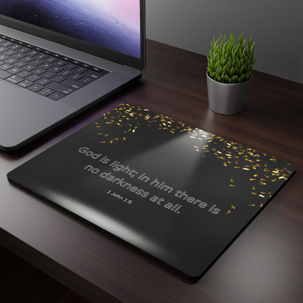 Black God Is Light mouse pad with inspirational Bible verse and gold confetti design next to laptop and plant on wooden desk