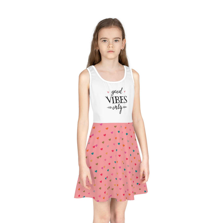 Girl wearing a mid-length sleeveless sundress with a white top featuring "good vibes only" text and a pink A-line skirt with colorful heart patterns