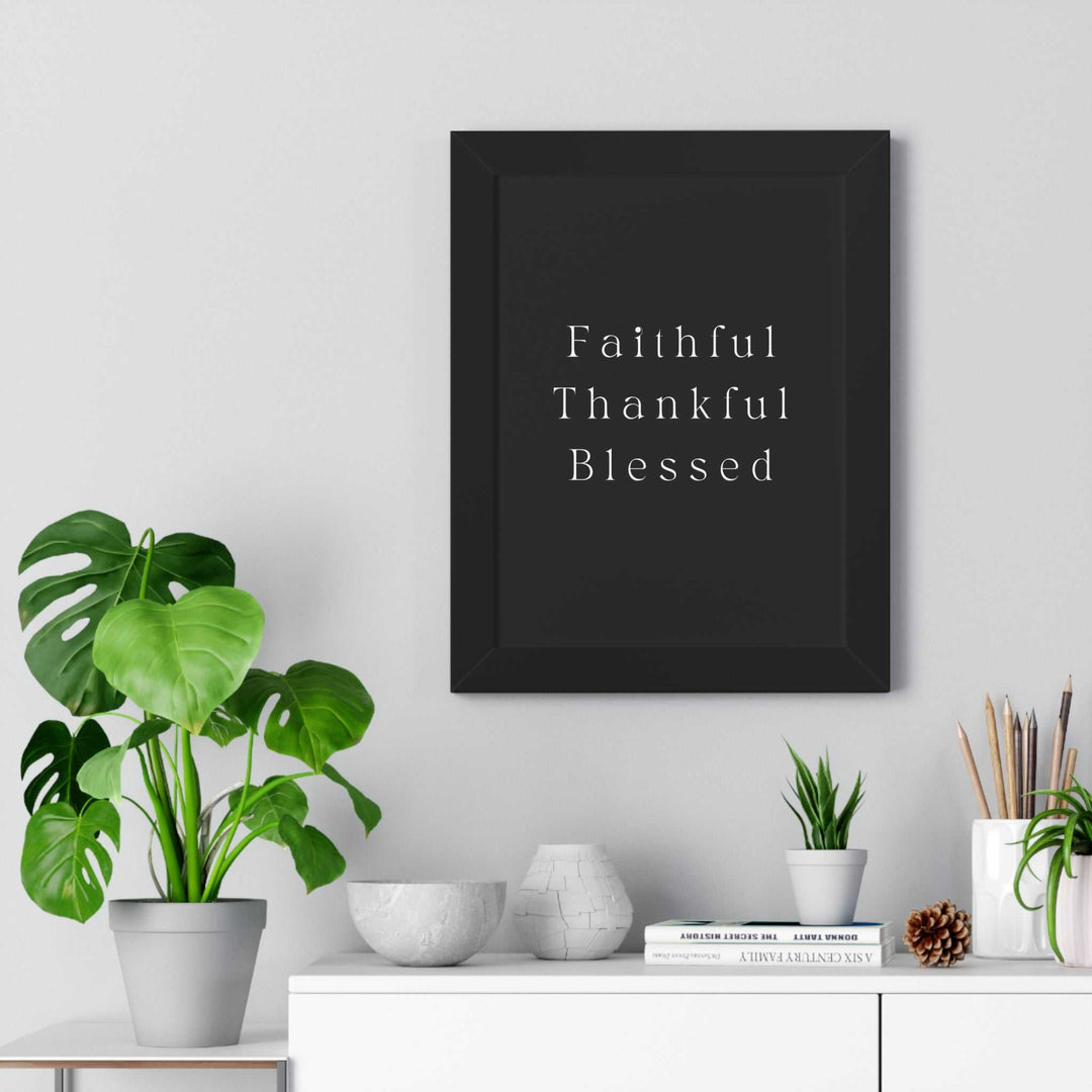 Black framed poster with white text reading "Faithful Thankful Blessed" hanging on a wall above a white shelf with plants and decor items