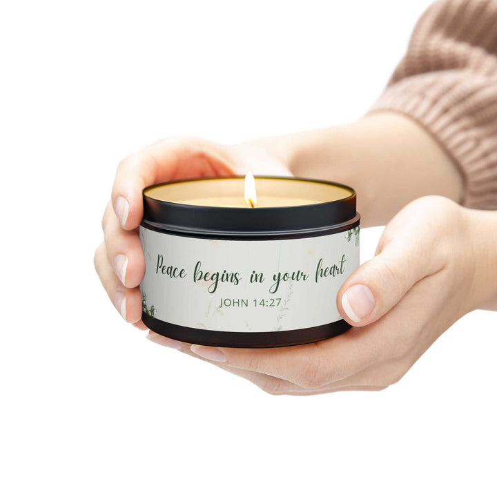 Hand holding a lit John 14:27 tin candle with peace-themed label