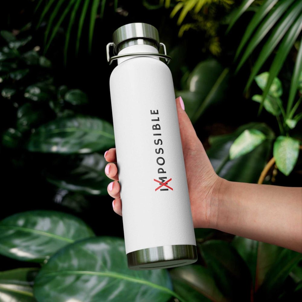 White Tout Est Possible bottle with metal lid, held in hand against green leafy background, featuring motivational design and spill-proof, BPA-free build