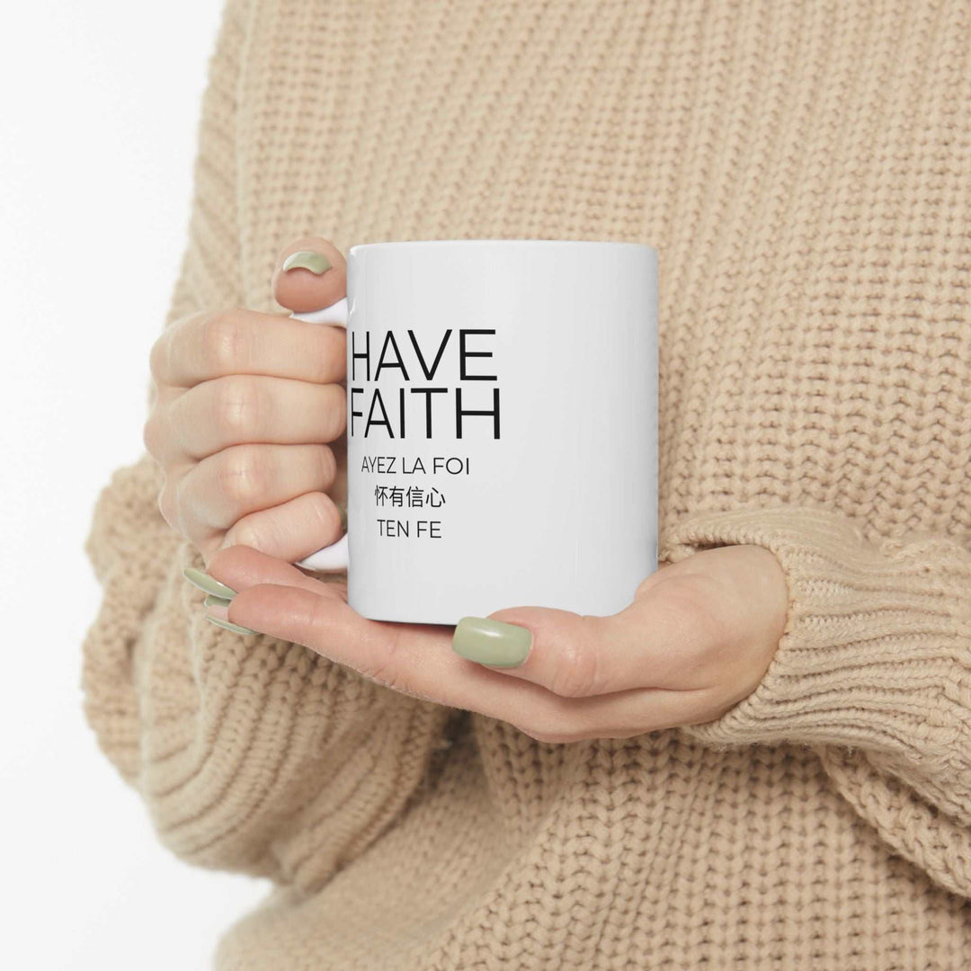 White ceramic Have Faith mug with black text held by person wearing beige sweater, shiny finish and C-handle design