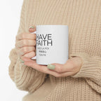 White ceramic Have Faith mug with shiny finish and comfortable C-handle held by person in beige sweater