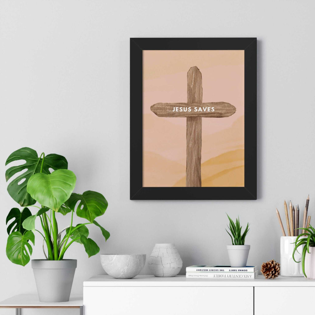 Framed Jesus Saves poster with wooden cross design displayed on a gray wall above a white shelf with plants and decor items.