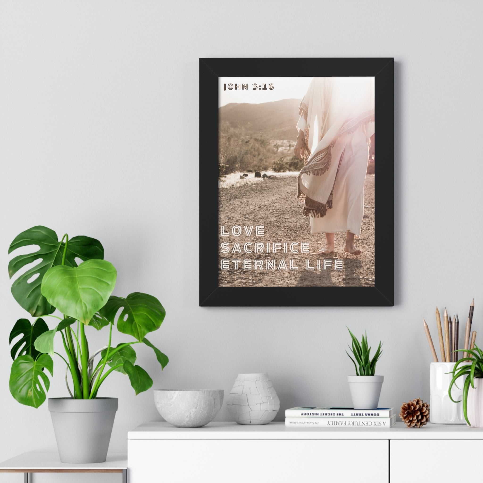 John 3:16 poster with love sacrifice eternal life text in a black frame on wall above a shelf with plants and decor