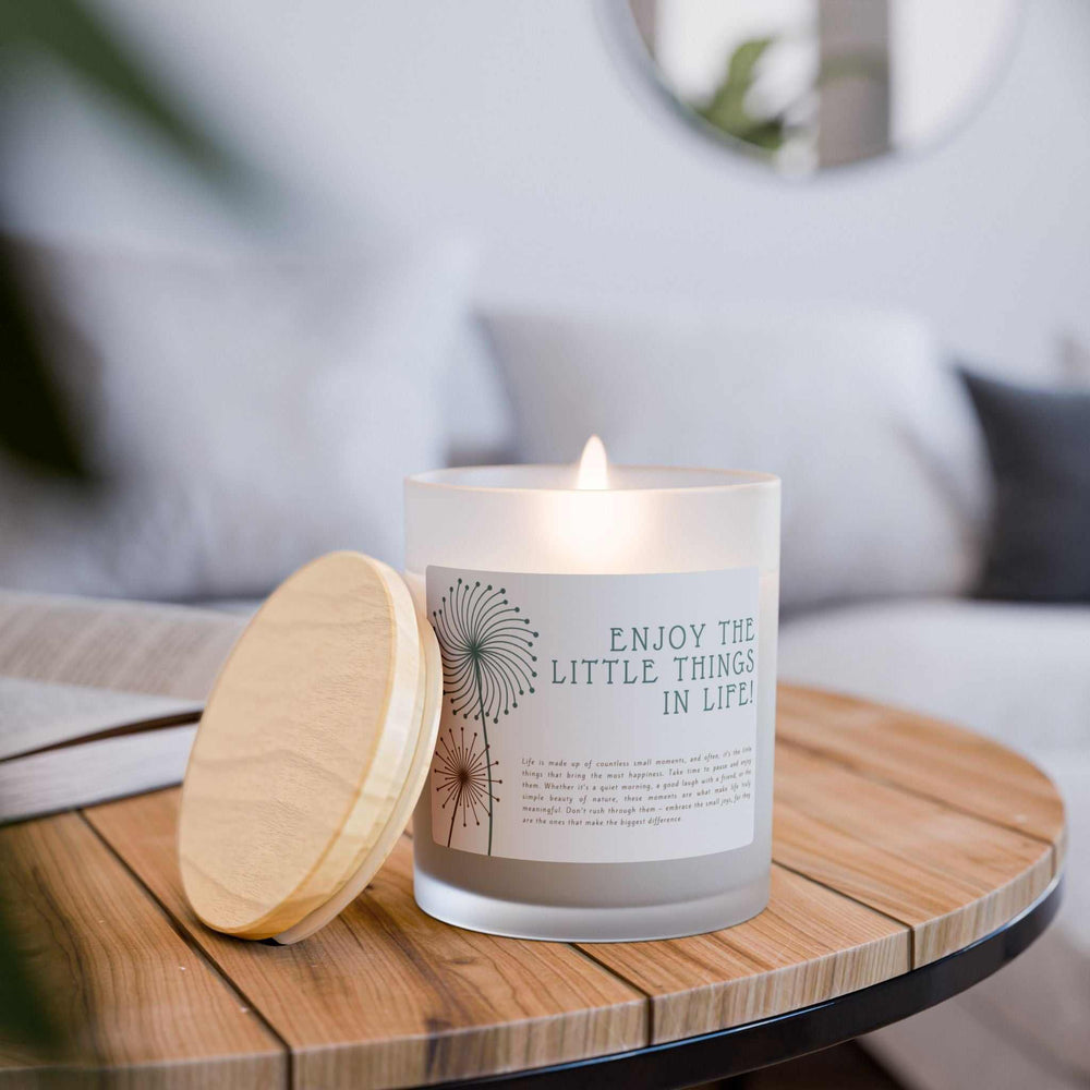 Lit frosted glass candle with raw maple lid on wooden table, natural off-white coconut soy wax candle labeled "Enjoy the Little Things in Life"