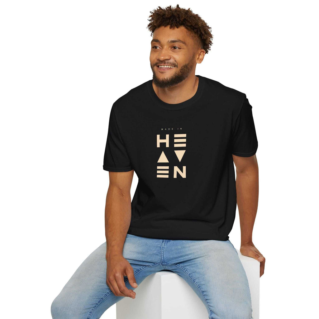 Black Heaven T-shirt with beige text worn by smiling man in light blue jeans sitting on white cube