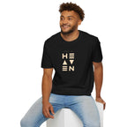 Black Heaven T-shirt with beige text worn by smiling man in light blue jeans sitting on white cube