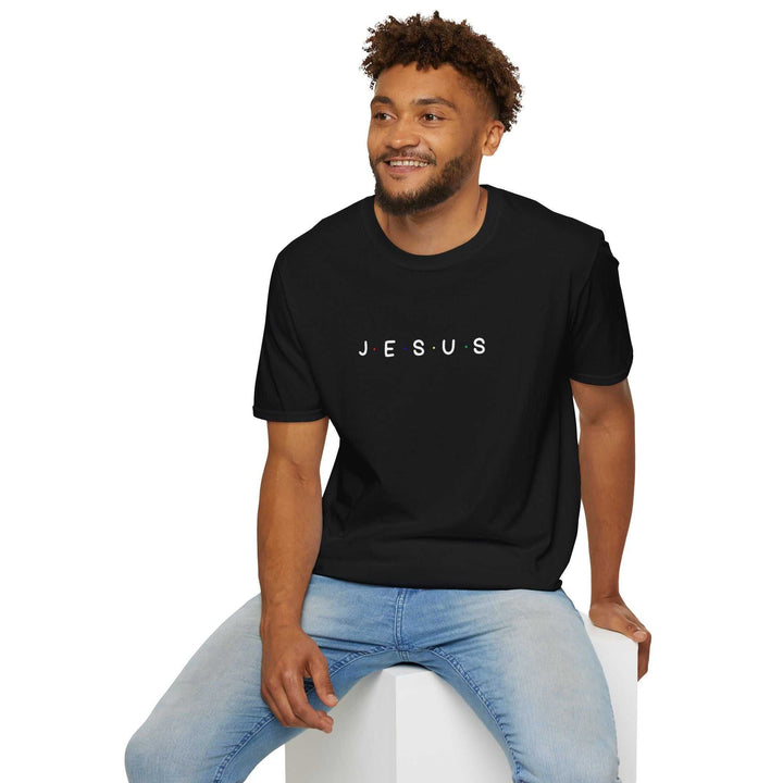 Man wearing black Jesus T-shirt with white text and light blue jeans, sitting on a white block