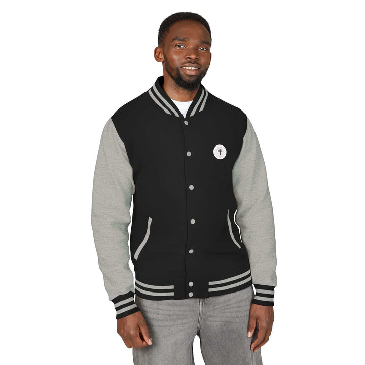 Man wearing Christian Cross varsity jacket with black body and gray sleeves, featuring a small cross emblem on the chest, striped collar, cuffs, and hem.