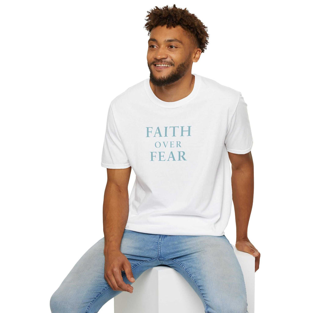 Man wearing white Faith Over Fear T-shirt with blue text and light blue jeans sitting on white block