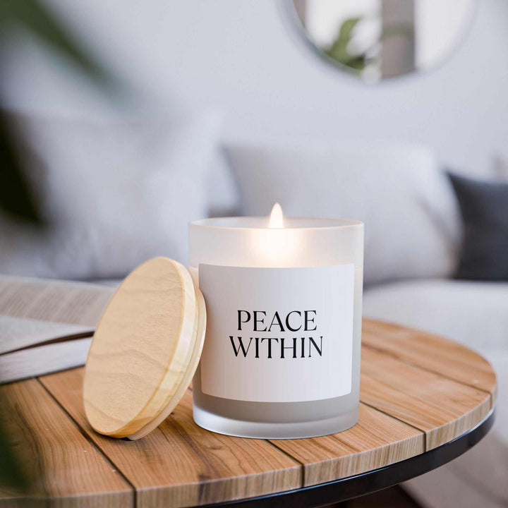 Lit Peace Within glass candle with wooden wick on wooden table, cozy home decor.