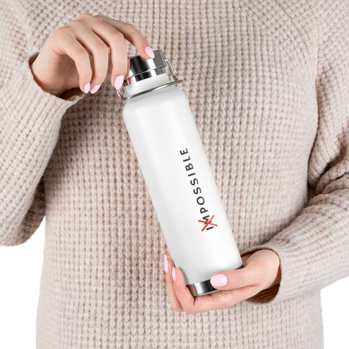 White stainless steel Tout Est Possible bottle with spill-proof cap held by person in beige sweater, featuring motivational design