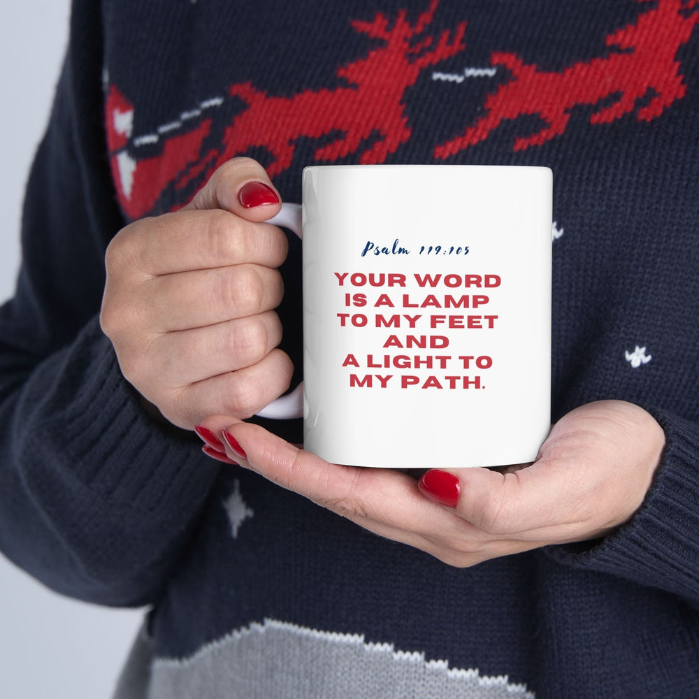 Person holding a white ceramic mug with Psalm 119:105 scripture in red and blue text on a navy sweater background
