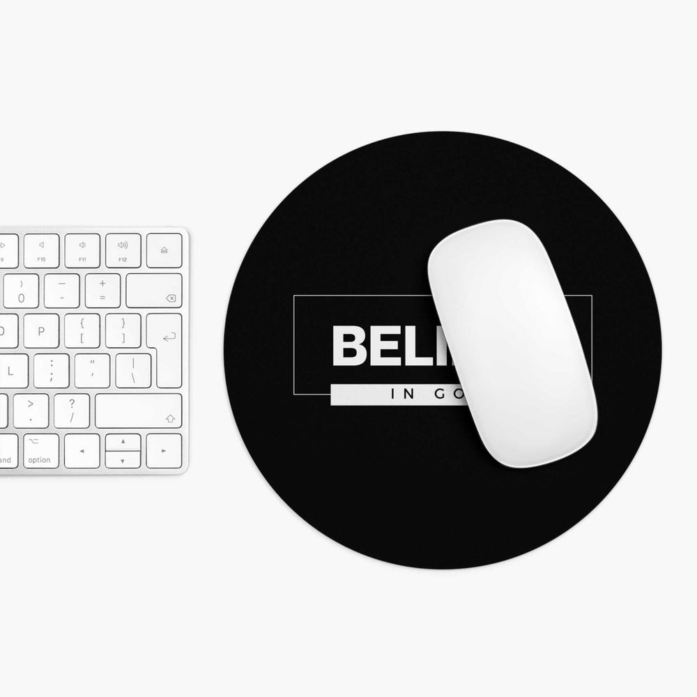 Black round mouse pad with "Believe In God" text and a white wireless mouse on top next to a white keyboard