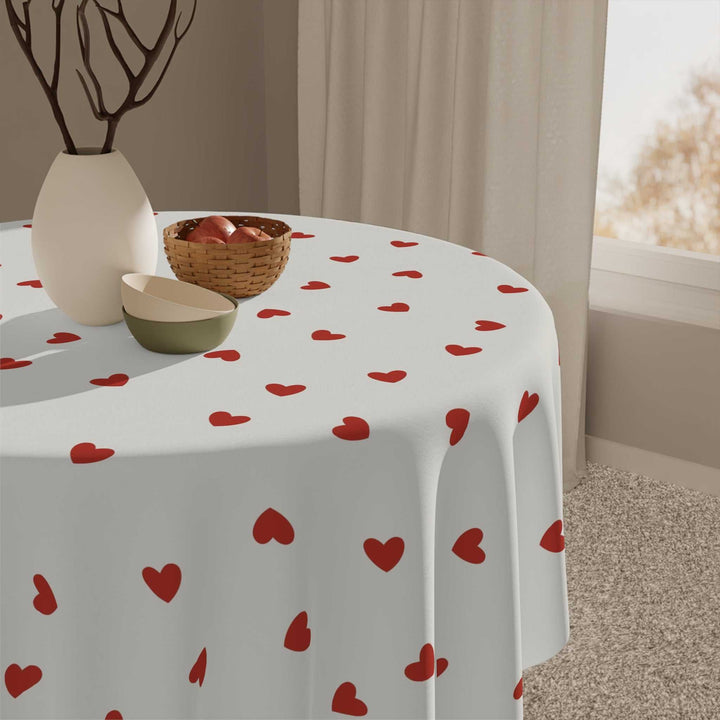 Round white tablecloth with red hearts pattern covering a dining table