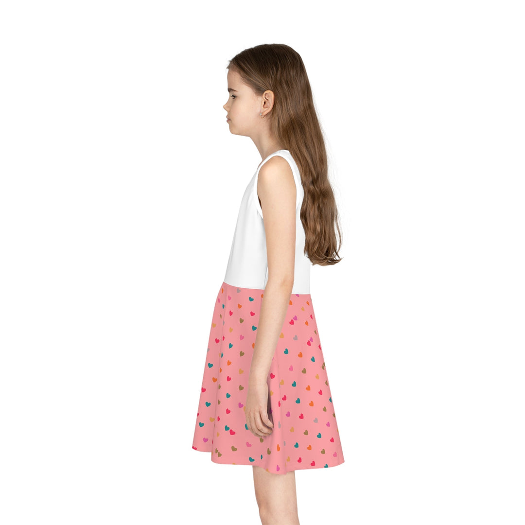 Girl wearing a mid-length sleeveless sundress with a white top and pink A-line skirt with colorful heart patterns