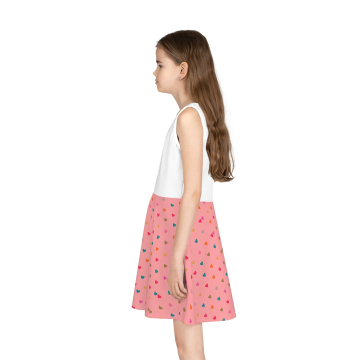 Girl wearing a mid-length sleeveless sundress with a white top and pink A-line skirt with colorful heart patterns