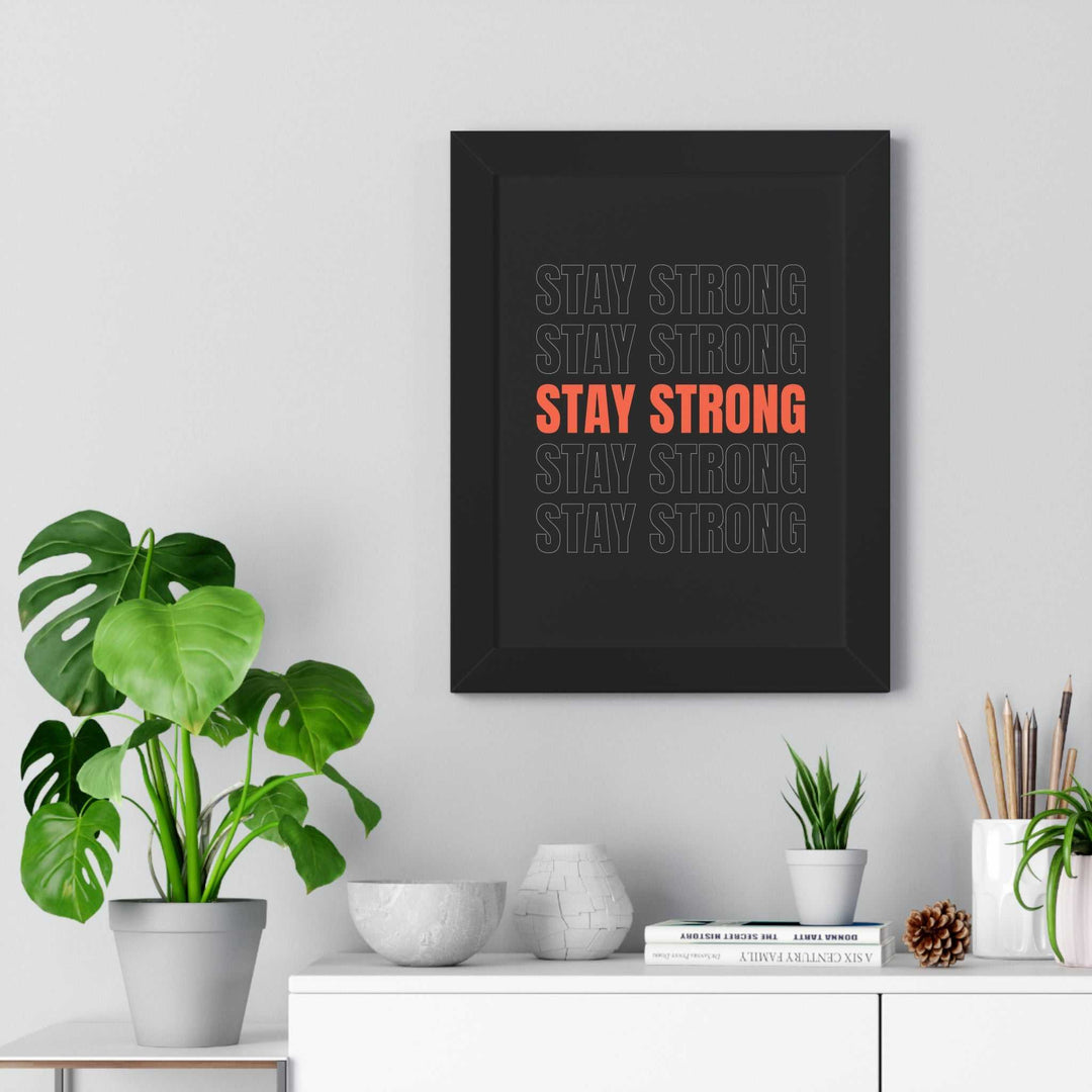 Stay Strong framed motivational poster with bold black and orange design hanging on wall above white cabinet with plants and decor