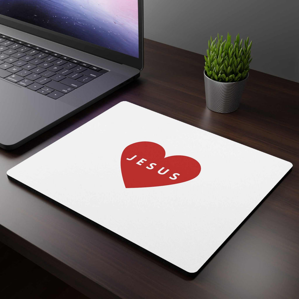 White Jesus Mouse Pad with red heart design on wooden desk next to laptop and small green plant