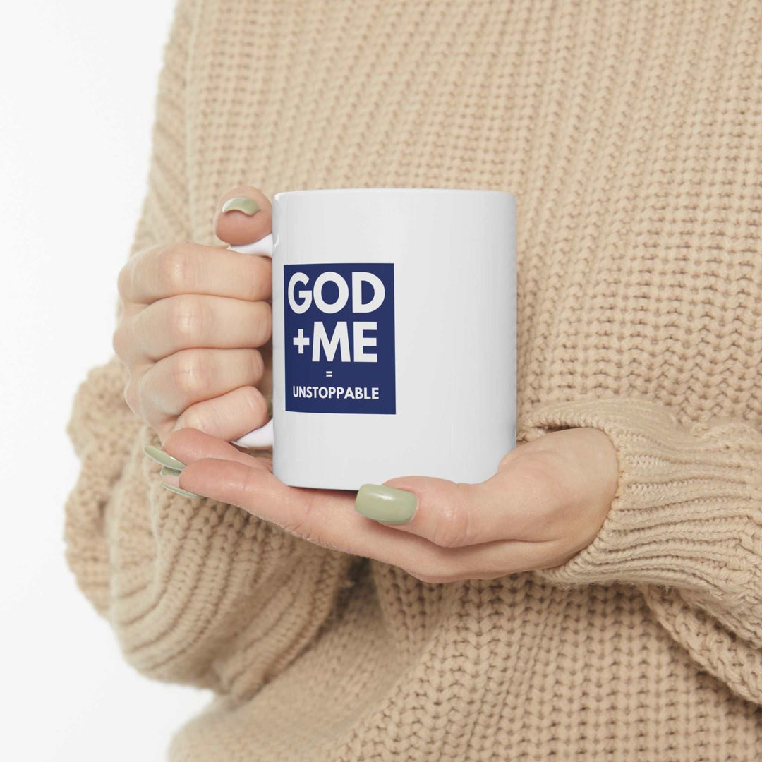 White ceramic mug with "GOD + ME = UNSTOPPABLE" faith-based design held by person wearing beige sweater, 11oz capacity, dishwasher and microwave safe mug
