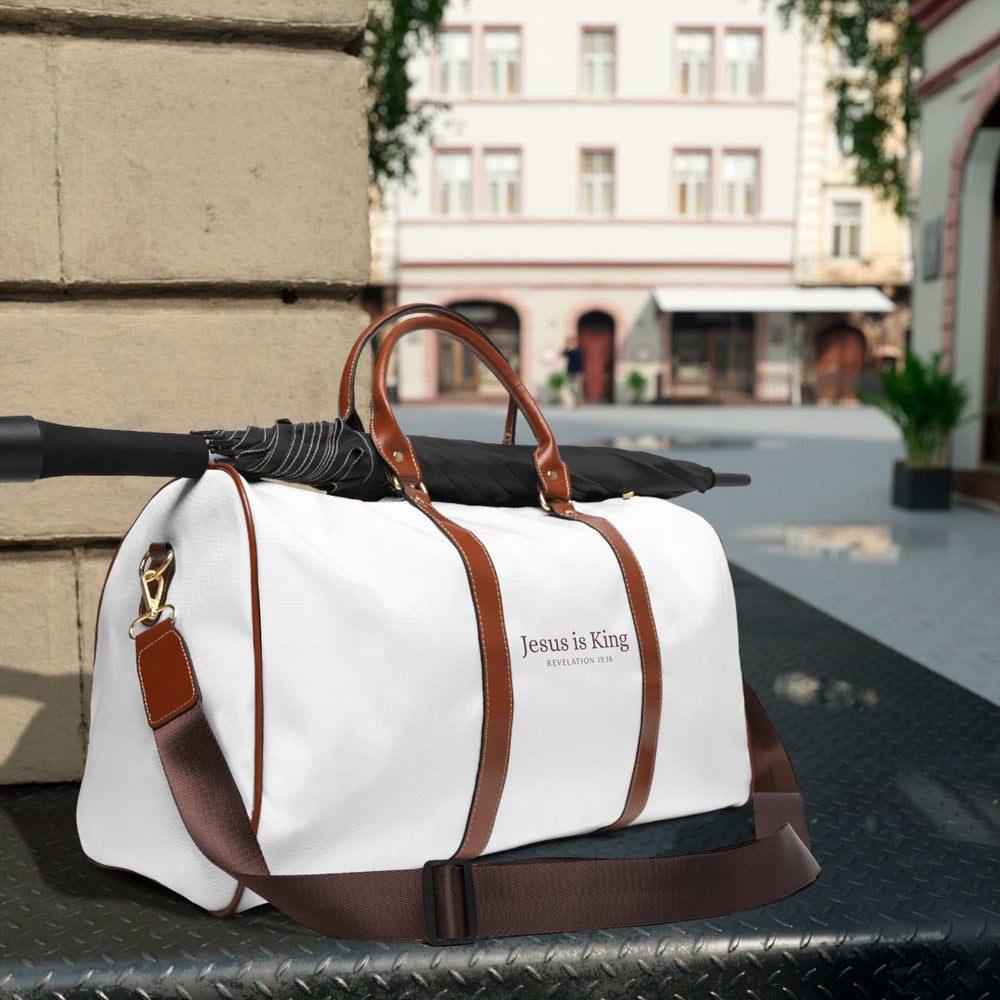 White Jesus is King travel bag with brown PU leather handles and adjustable shoulder strap, gold zipper, and durable nylon material.