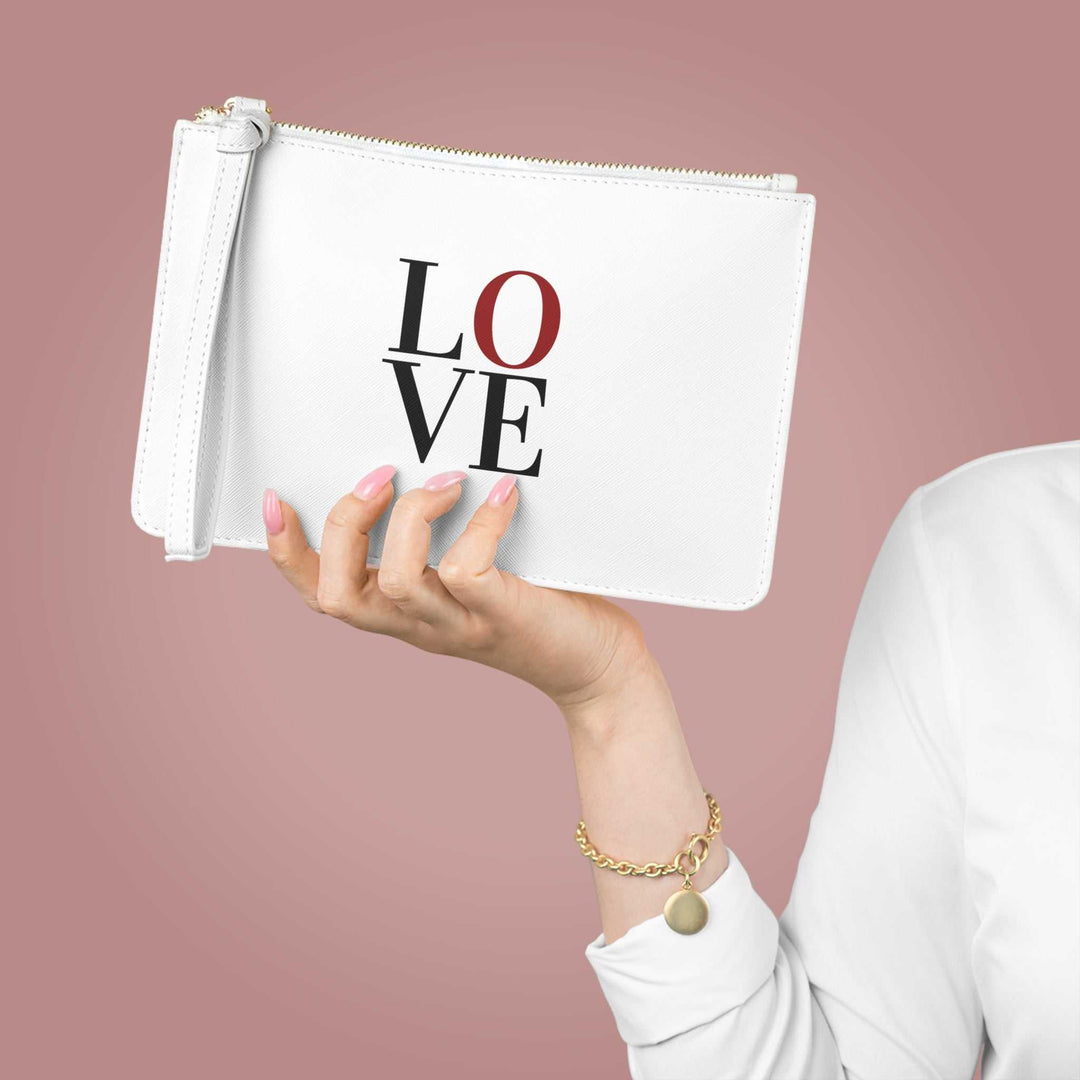 White Love Clutch Bag with wrist strap and saffiano finish held in hand against pink background