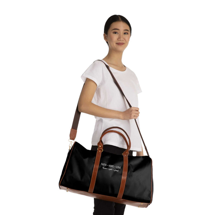 Woman carrying black Faith Hope Love travel bag with brown PU leather handles and adjustable shoulder strap