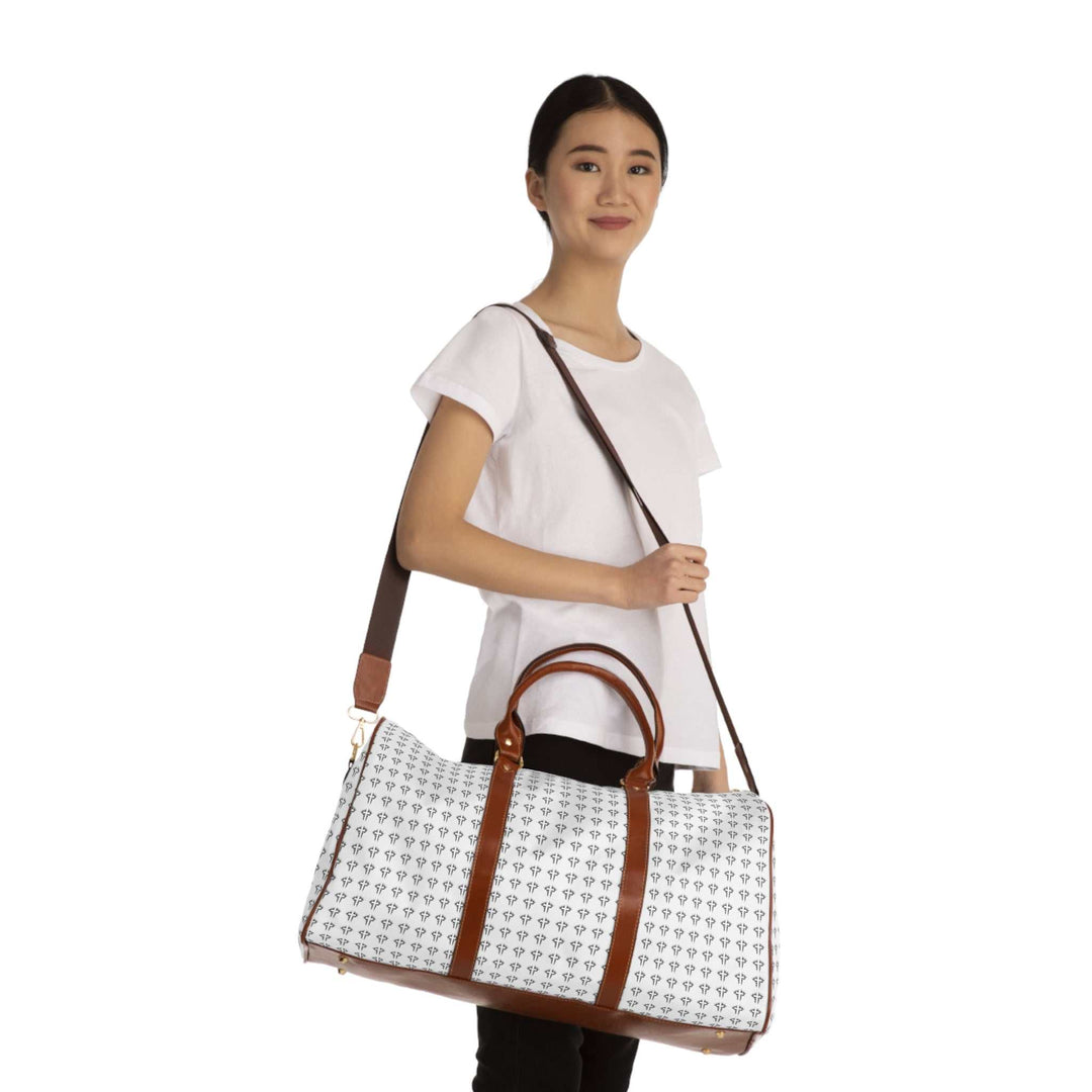 Christian Cross travel bag with brown PU leather handles and adjustable shoulder strap, white patterned nylon body, and gold zipper held by woman in white t-shirt