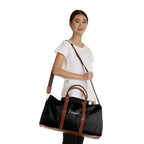 Black Blessed travel bag with brown PU leather handles and adjustable shoulder strap worn by woman