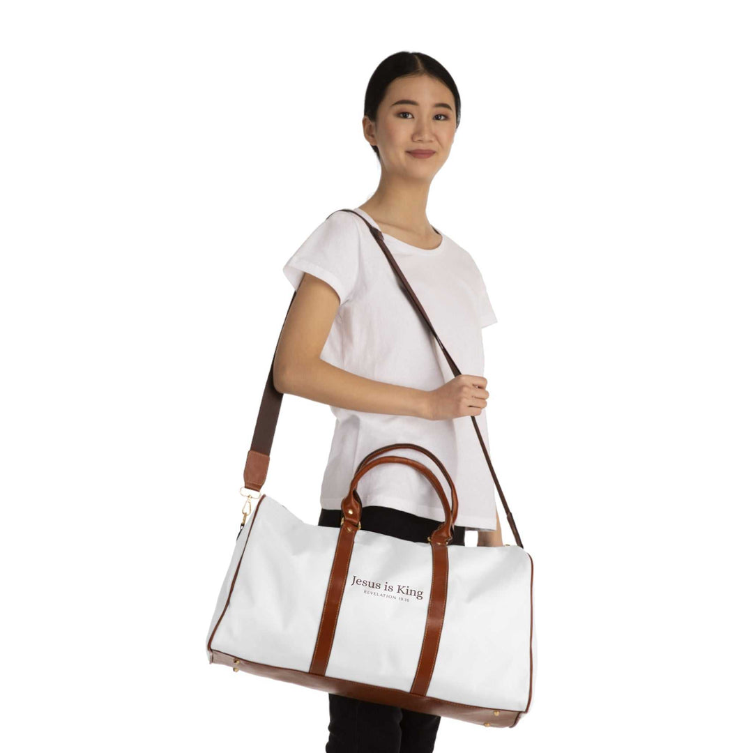 White and brown Jesus is King travel bag with gold zipper, carried by a woman wearing a white t-shirt