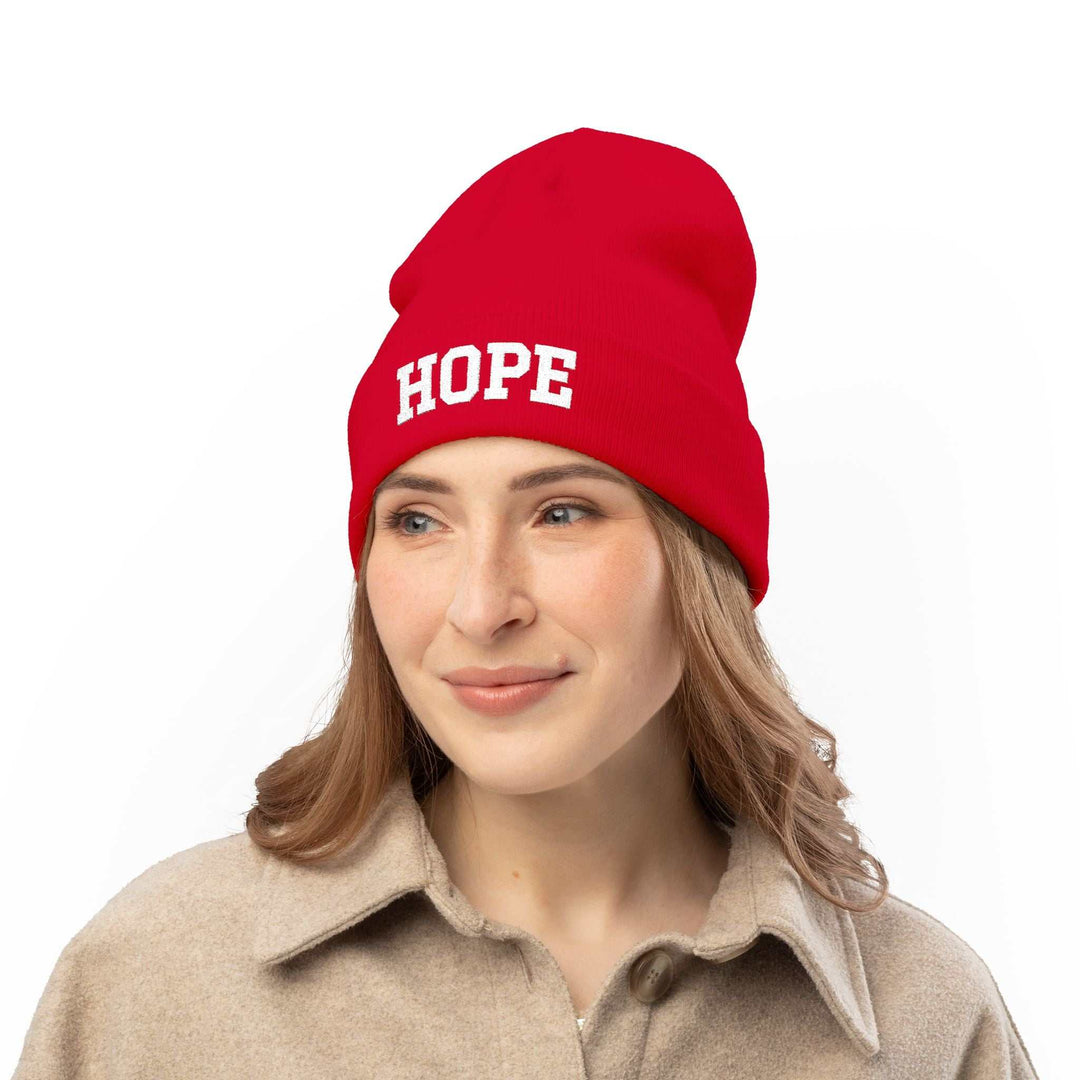 Woman wearing a red knit beanie with "HOPE" text in white, styled with a beige coat.